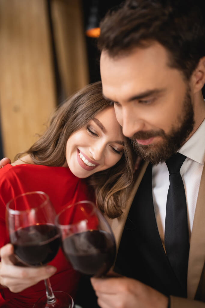 boldog nő és szakállas férfi kattogó szemüveg vörösborral ünneplés közben Valentin-napon  - Fotó, kép