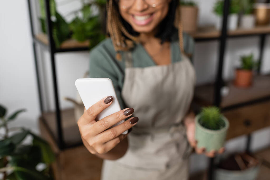 partial view of smiling african american woman holding smartphone during video call in flower shop - Photo, Image