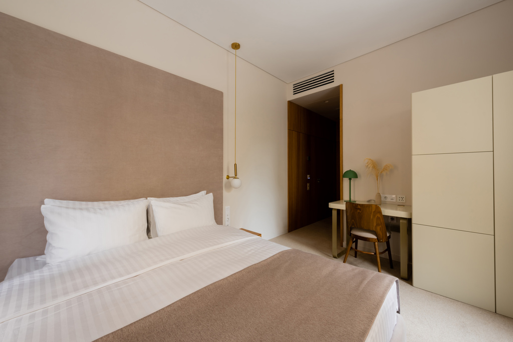 άνετο κρεβάτι με λευκά κλινοσκεπάσματα κοντά στο γραφείο και ξύλινη καρέκλα στο σύγχρονο υπνοδωμάτιο του ξενοδοχείου - Φωτογραφία, εικόνα