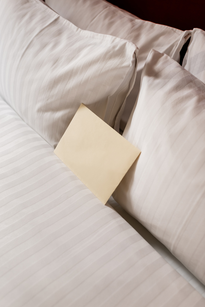 high angle view of blank envelope on white and clean bedding in hotel room  - Fotó, kép