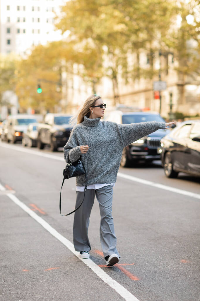 longitud completa de la mujer con estilo en gafas de sol y traje gris sosteniendo bolso y la captura de la cabina en la calle de Nueva York - Foto, Imagen