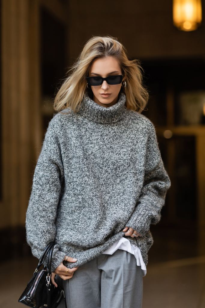 mujer con estilo en gafas de sol y suéter gris caminando con bolso negro en Nueva York  - Foto, imagen