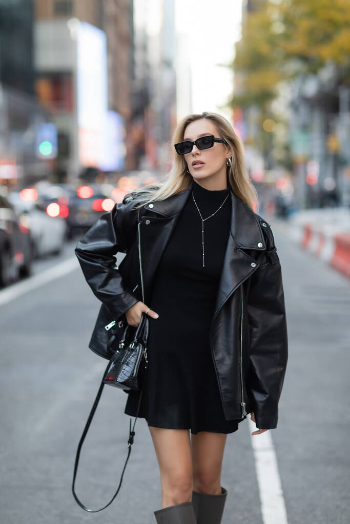ニューヨークの路上でヒップに手で立って革のジャケットと黒のドレスのスタイリッシュな女性  - 写真・画像