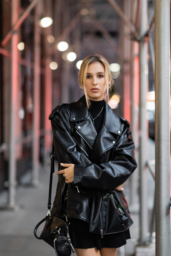 junge blonde Frau in schwarzer Lederjacke steht abends auf der Straße in New York City - Foto, Bild