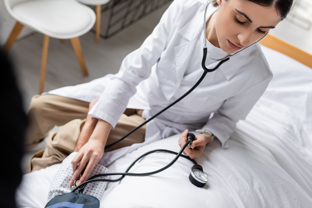 Wysoki kąt widzenia lekarza sprawdzającego ciśnienie krwi pacjenta w podeszłym wieku na łóżku w szpitalu  - Zdjęcie, obraz