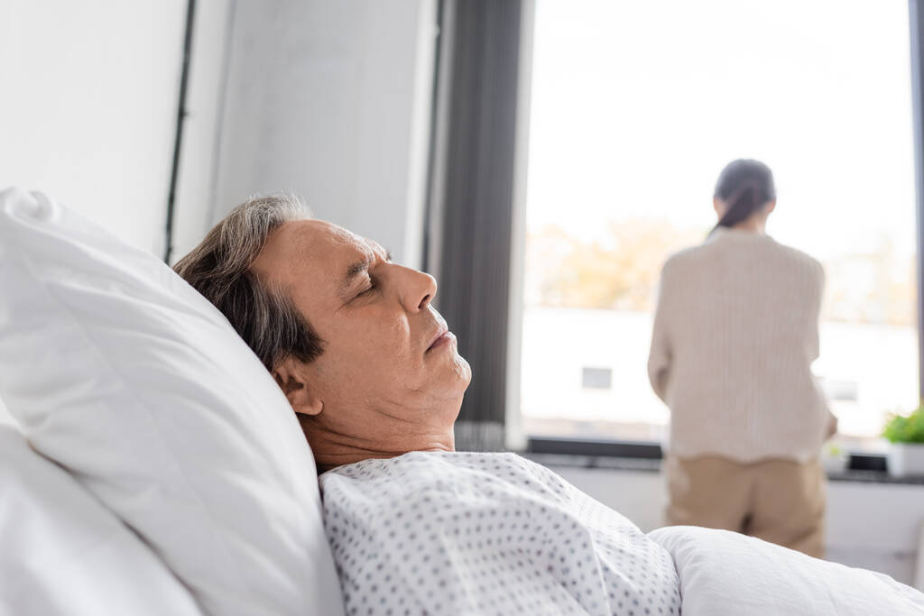 Senior man lying on bed near blurred daughter in hospital ward  - Foto, imagen