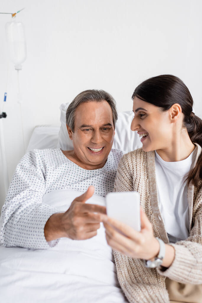 Позитивный пациент указывает на смартфон рядом с дочерью в больнице  - Фото, изображение