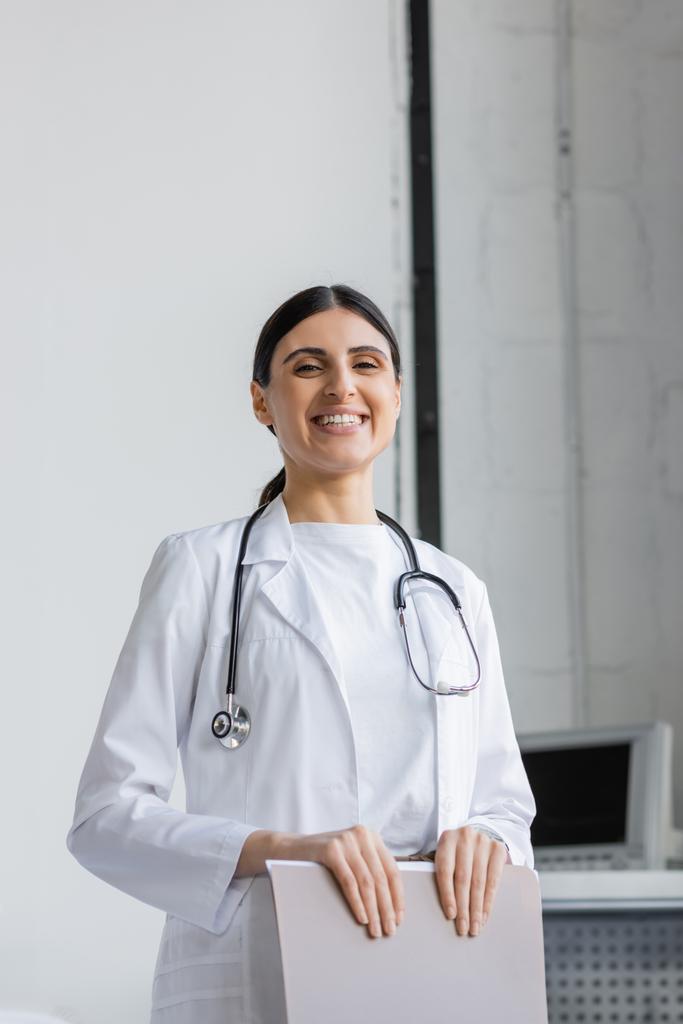 Fröhlicher Arzt hält Papiermappe auf Krankenhausstation  - Foto, Bild