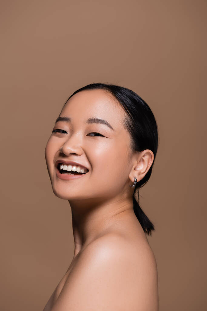 Positive asian model with naked shoulder looking at camera isolated on brown  - Fotoğraf, Görsel