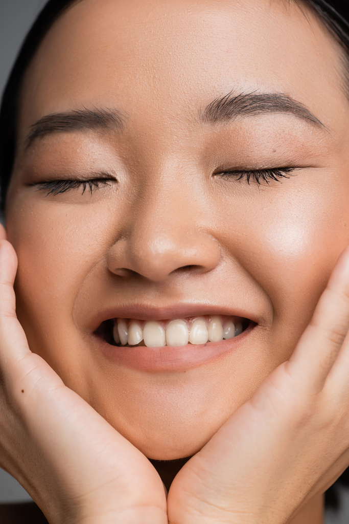 close up portrait of smiling asian woman with natural makeup touching face while smiling with closed eyes - Fotografie, Obrázek