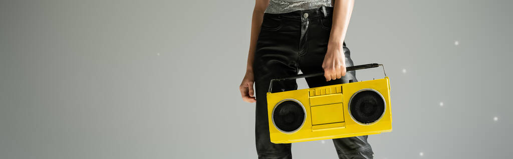 cropped view of woman in black leather pants holding boombox on grey background, banner - Fotó, kép