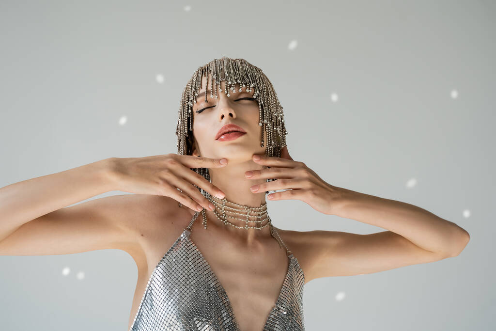 Trendy young woman in jewelry headwear touching chin on grey background with light  - Fotoğraf, Görsel