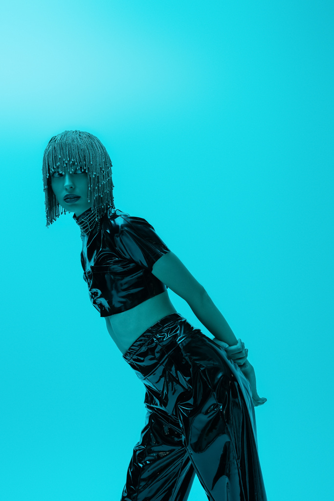 Модна жінка в розкішному одязі для голови та латексу дивиться ізольовано на синьому фоні з освітленням
 - Фото, зображення