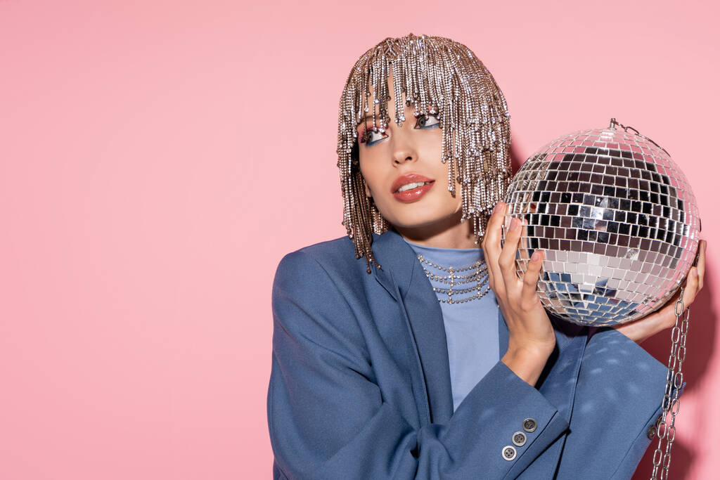 Trendy young woman in jewelry headwear holding disco ball on pink background  - Fotó, kép
