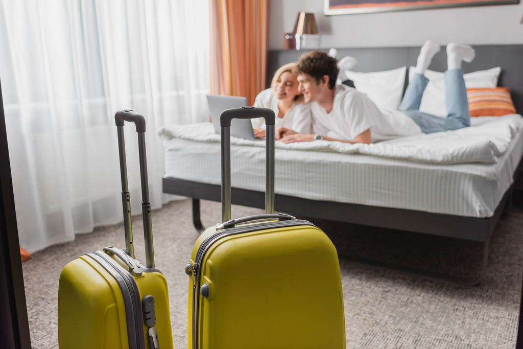 selective focus of suitcases near young travelers watching movie on laptop in modern hotel bedroom - Foto, afbeelding