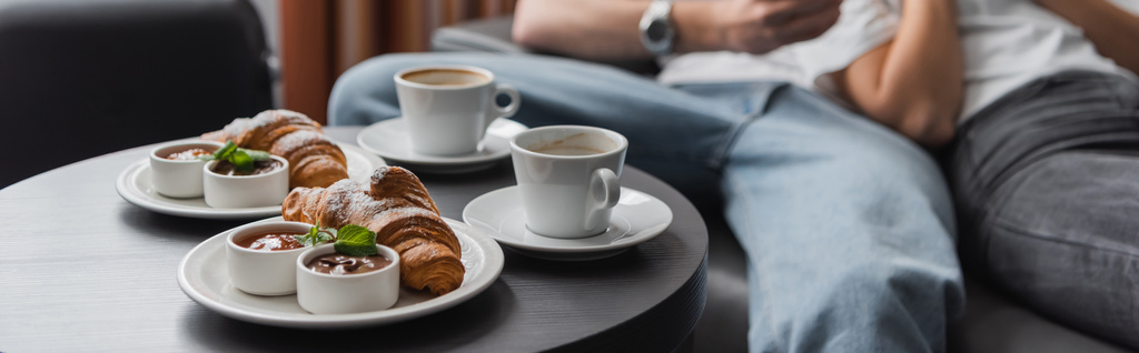 tasty croissants with jam and chocolate paste near coffee cups and cropped couple on blurred background, banner - Photo, image