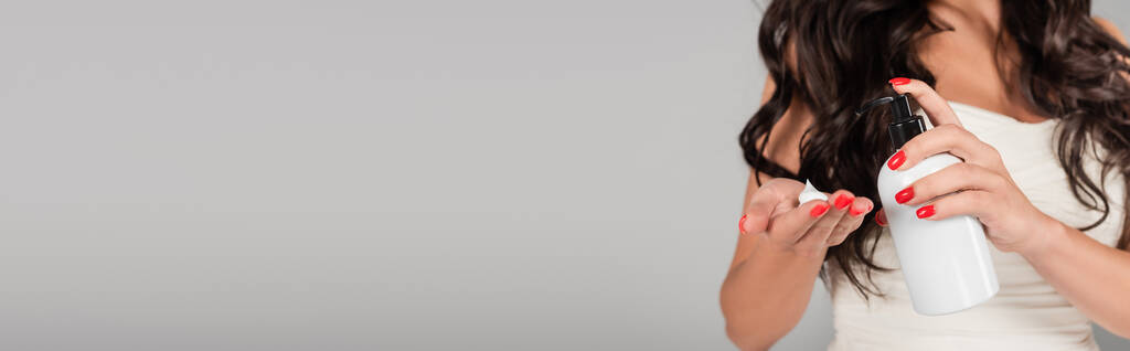 μερική άποψη της μελαχρινής γυναίκας με μακριά μαλλιά εφαρμογή αφρού styling στο χέρι απομονώνονται σε γκρι, πανό - Φωτογραφία, εικόνα
