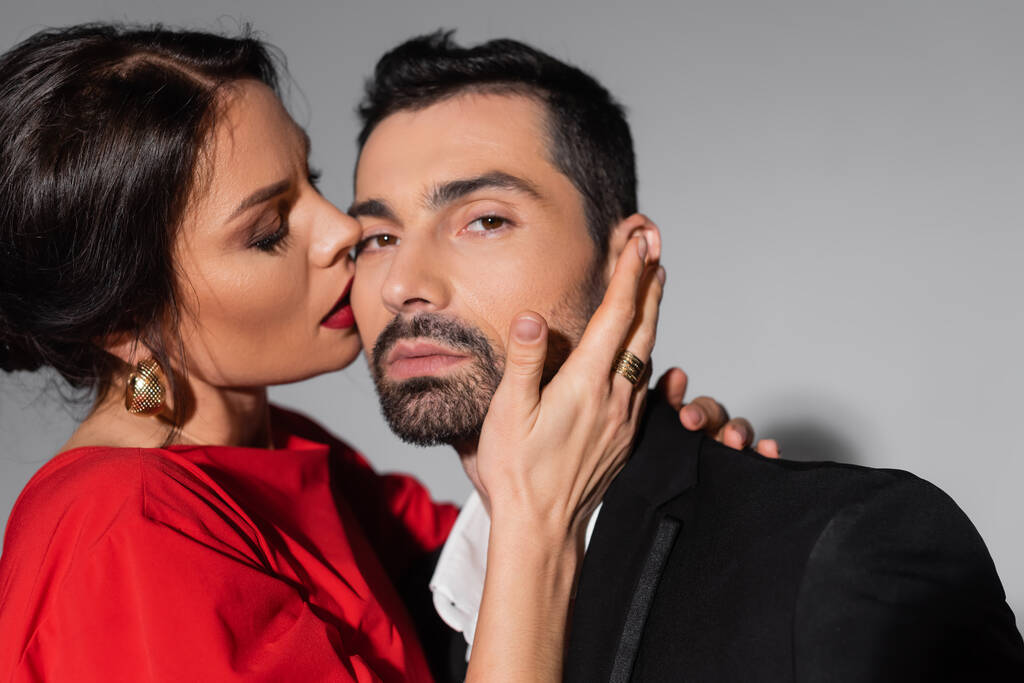 Elegant woman with makeup kissing boyfriend in formal wear on grey background  - Fotó, kép