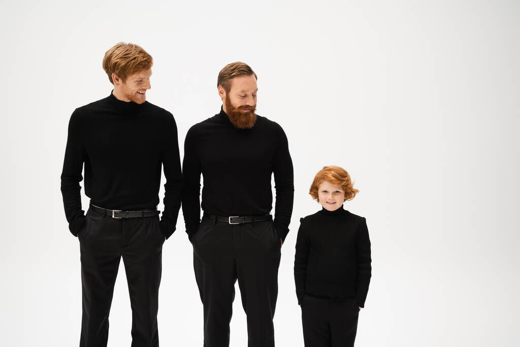 redhead bearded men and cheerful boy in black clothes standing with hands in pockets isolated on grey - Zdjęcie, obraz