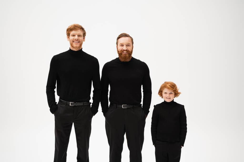 happy bearded men and red haired boy in black clothes posing with hands in pockets isolated on grey - Foto, Bild