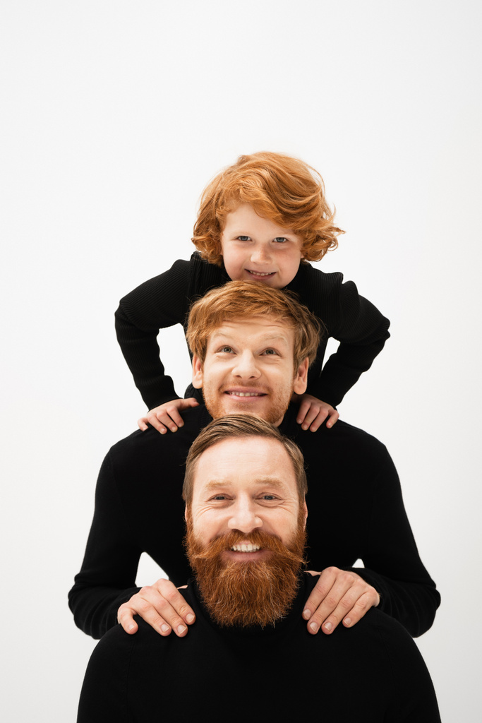 joyful redhead kid posing with smiling and bearded grandpa and dad in black turtlenecks isolated on grey - Photo, Image