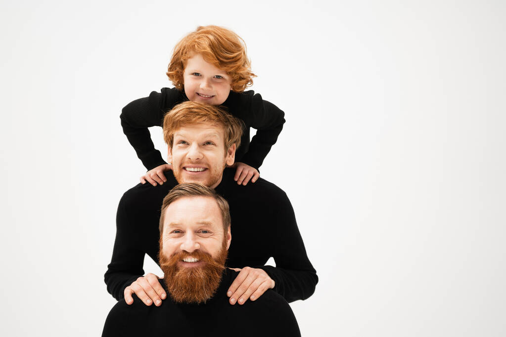 Kızıl saçlı, sakallı, siyah kazaklı baba ve oğul. Gri renkli izole edilmiş neşeli çocukla poz veriyorlar. - Fotoğraf, Görsel