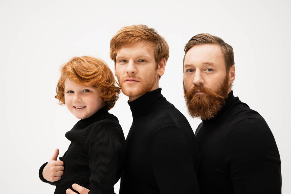 bearded men in black sweaters looking at camera near happy kid showing thumb up isolated on grey - Foto, Imagen