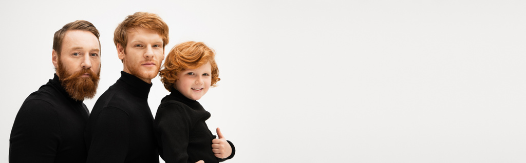 happy red haired boy showing thumb up near bearded grandpa and father in black turtlenecks isolated on grey, banner - Foto, Imagen