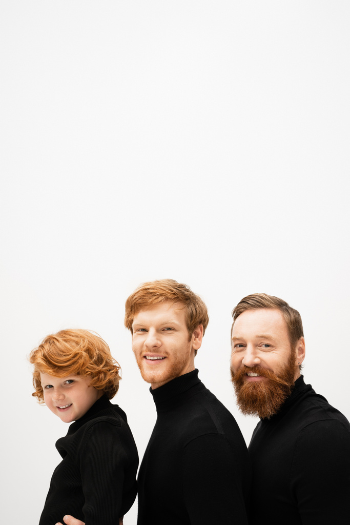 joyful bearded men and redhead boy in black turtlenecks smiling at camera isolated on grey - Foto, imagen