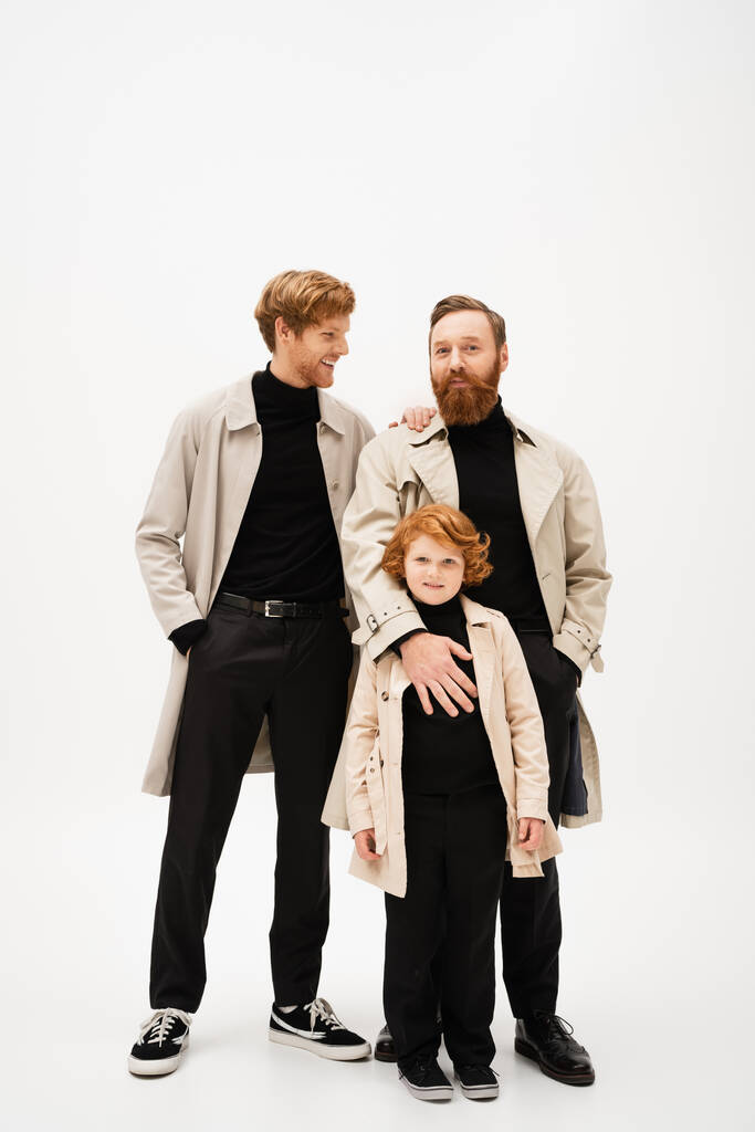 smiling man standing with hand in pocket near bearded dad and redhead son on light grey background - Fotó, kép