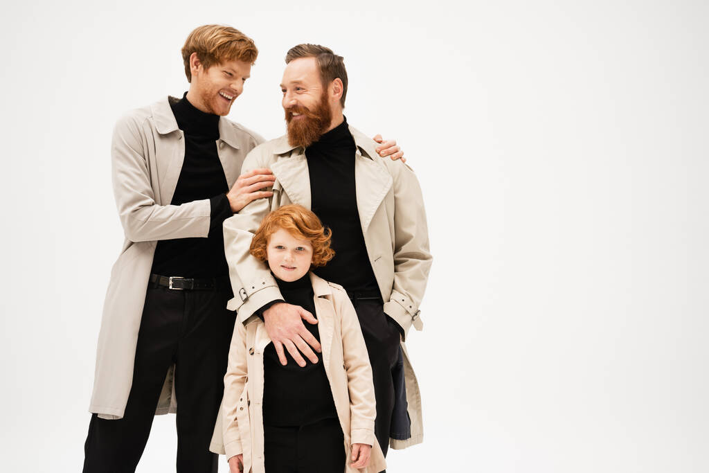 happy young man in trench coat hugging bearded father near redhead son isolated on grey - Foto, Imagen