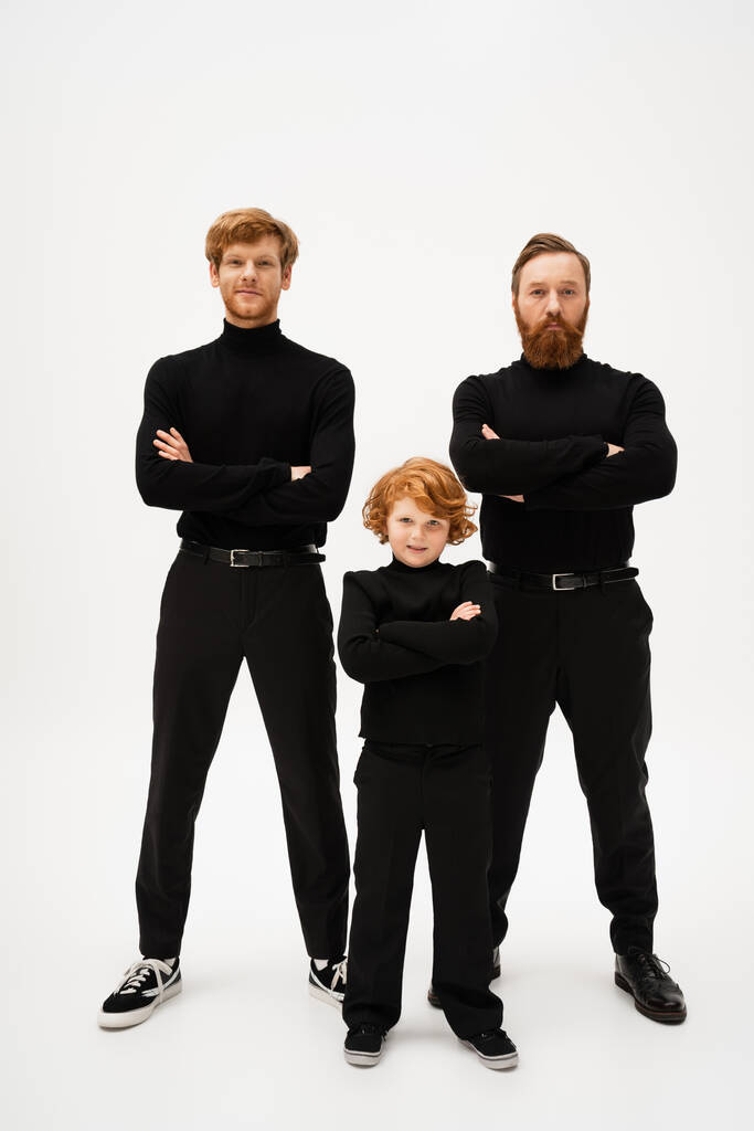 full length of bearded man with redhead son and smiling grandson posing with crossed arms on light grey background - Photo, image