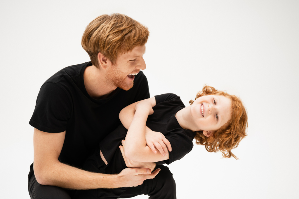 excited man in black t-shirt playing with happy redhead son crossing arms isolated on grey - Zdjęcie, obraz