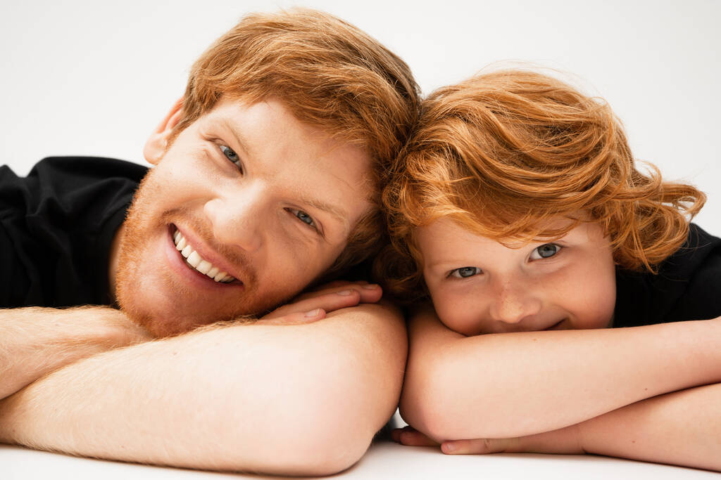 レッドヘッドの父親と息子が腕を組んで横になってカメラで笑っている姿を - 写真・画像