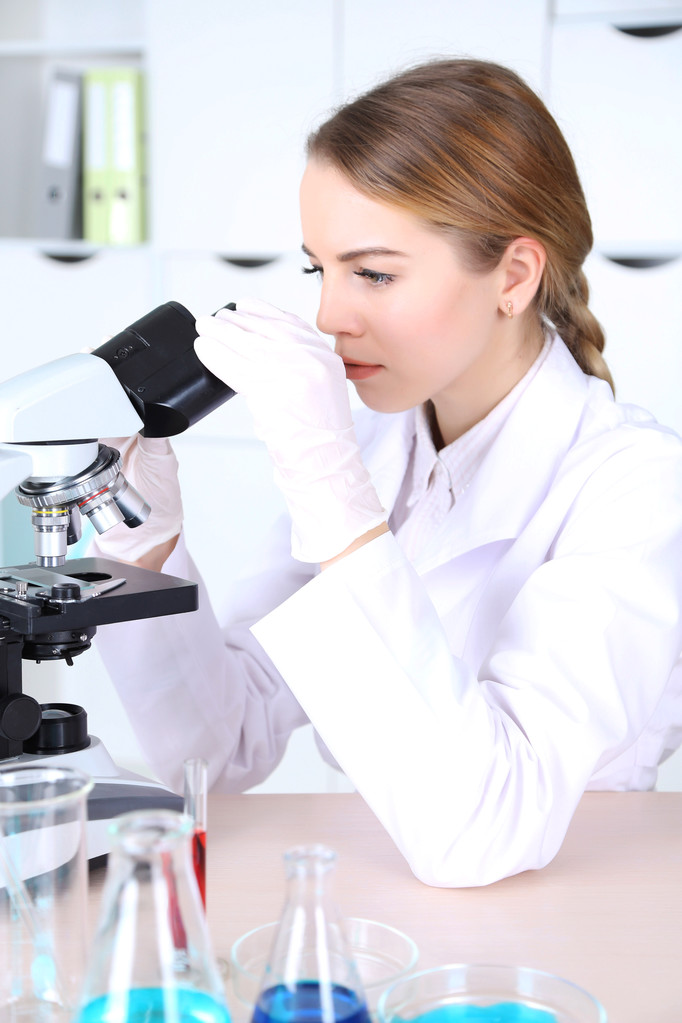 Nuori naispuolinen tiedemies mikroskoopilla laboratoriossa
 - Valokuva, kuva