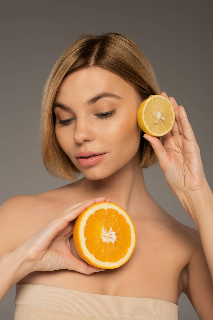 молода жінка тримає соковитий апельсин і кислий лимон ізольовані на сірому
  - Фото, зображення