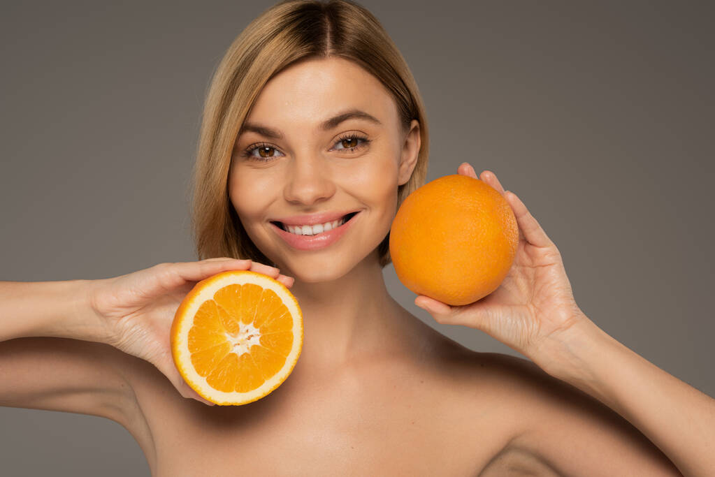 cheerful blonde woman holding juicy oranges isolated on grey  - Photo, Image