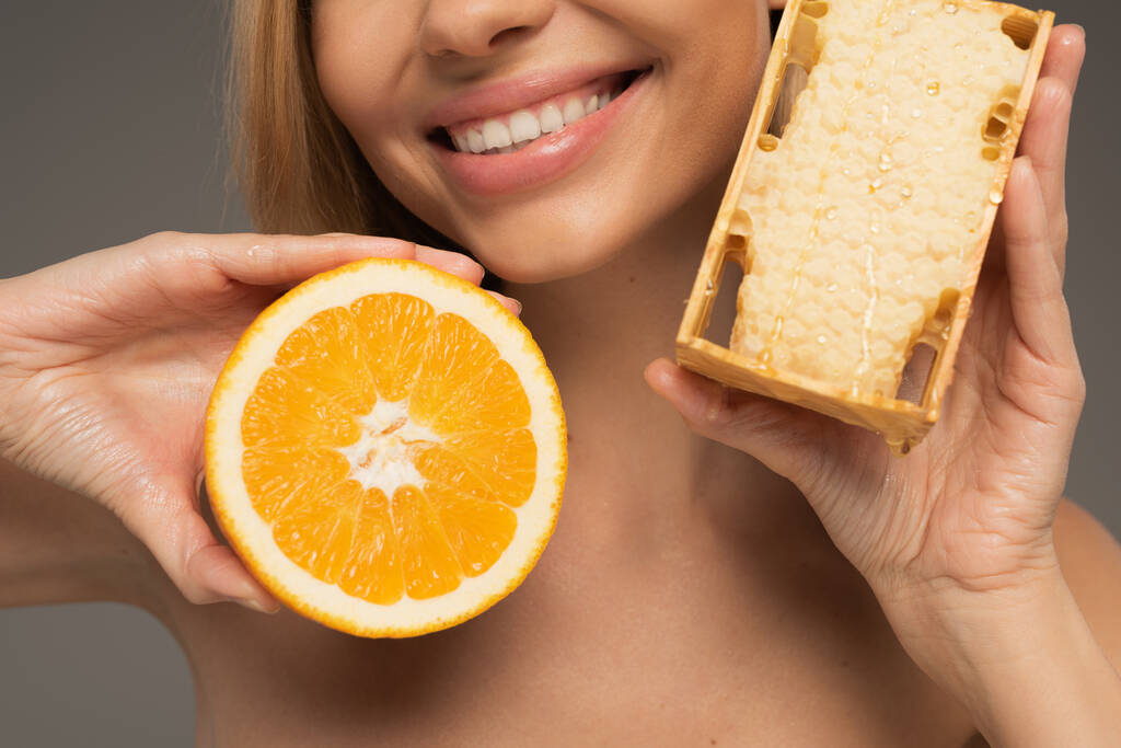 обрезанный вид счастливой женщины, держащей соты и оранжевые изолированы на серый  - Фото, изображение