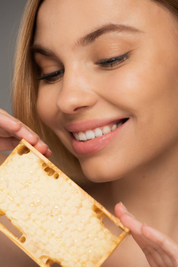 close up of happy woman holding sweet honey in honeycomb isolated on grey  - Foto, Bild