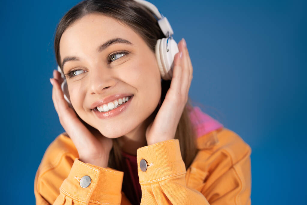 Portrait of joyful teenager in headphones looking away isolated on blue  - Foto, Imagen