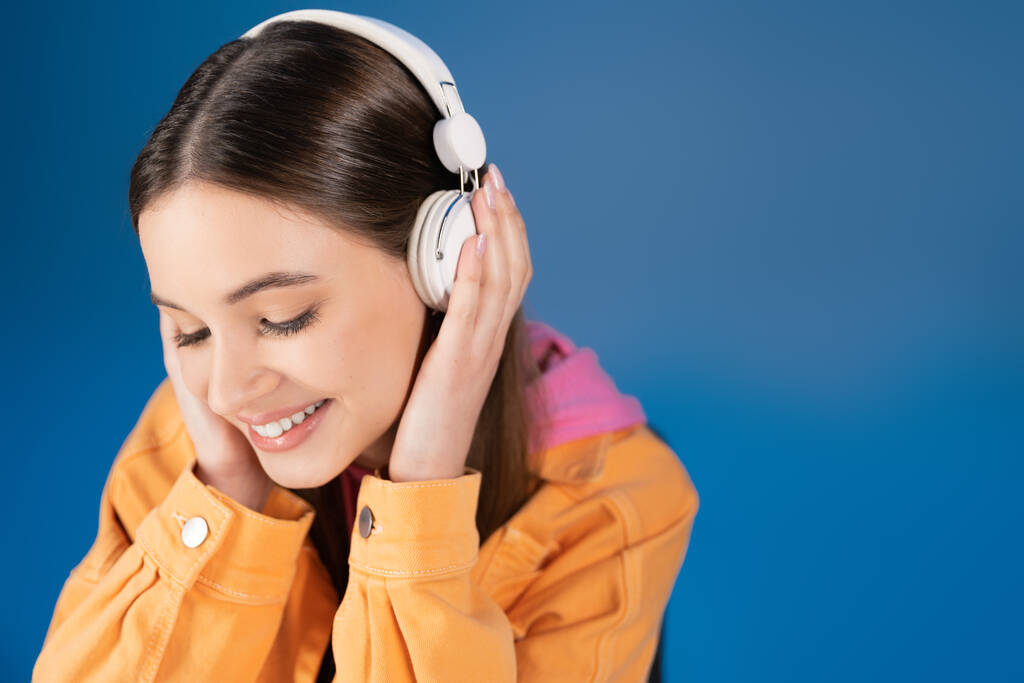 Pretty brunette teenager in headphones listening music isolated on blue  - Photo, image