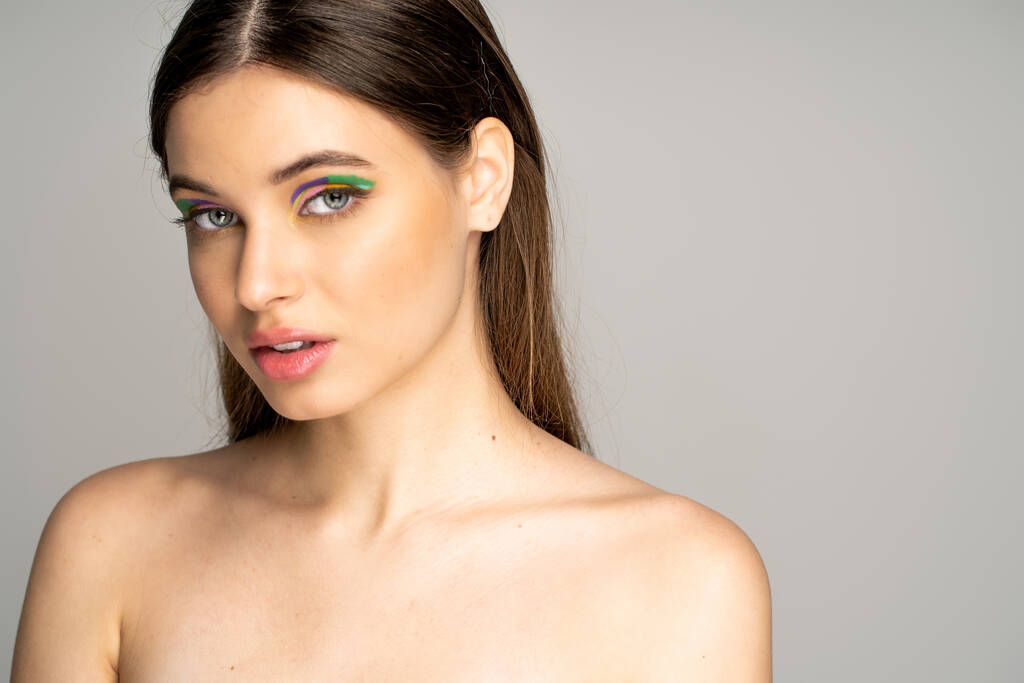 Burette teen girl with colorful eyeshadows and naked shoulders standing isolated on grey  - Foto, afbeelding