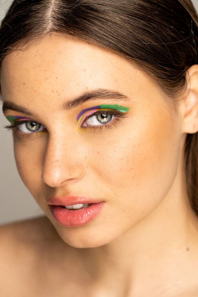 Teen model with colorful makeup and freckles looking at camera isolated on grey  - Foto, Imagen