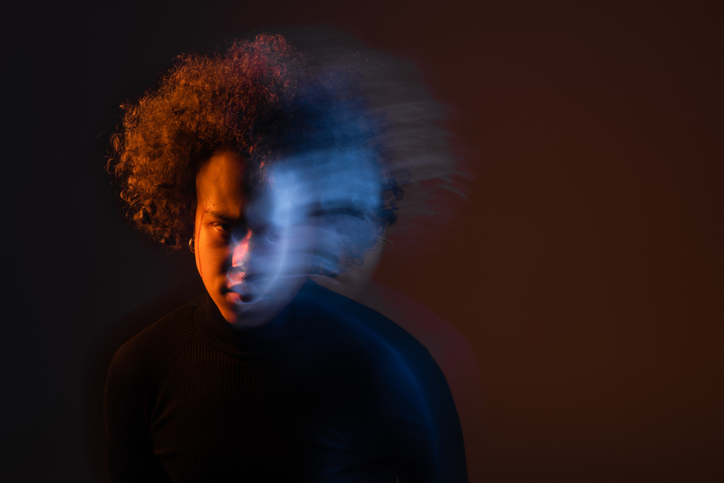 larga exposición del hombre afroamericano estresado con trastorno bipolar y cara sangrante sobre fondo oscuro con luz naranja y azul - Foto, imagen