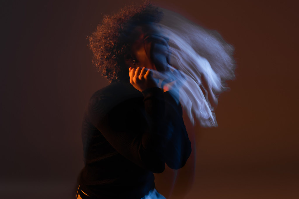 motion blur of young african american man with bipolar disorder on dark background with orange and blue light - Foto, Imagen