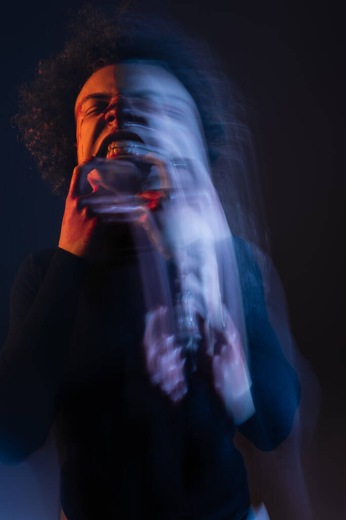exposição longa do homem americano africano ferido com transtorno bipolar e grimace irritado no preto com luz laranja e azul - Foto, Imagem