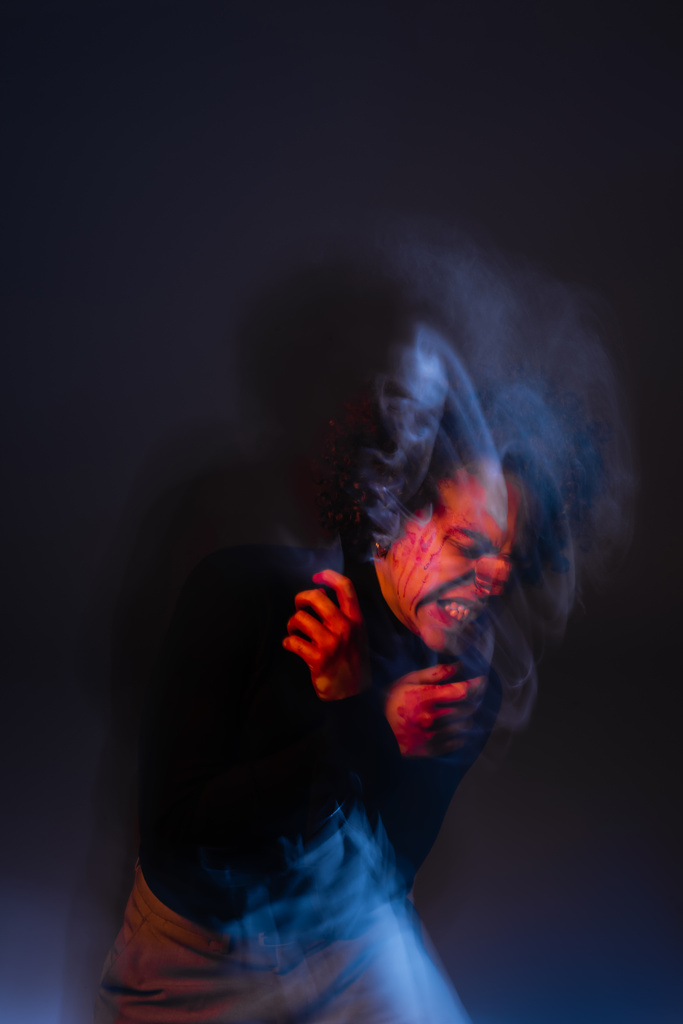 double exposure of stressed african american man with injured bleeding face grimacing on dark with red and blue light - Photo, Image