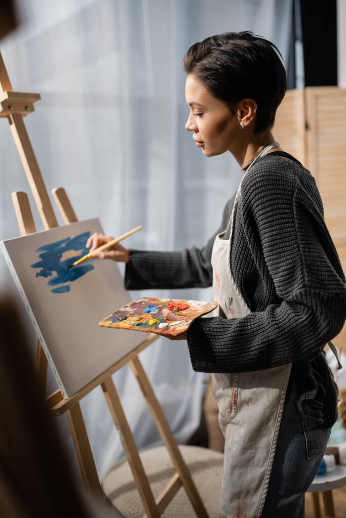 Side view of brunette artist painting on canvas in studio  - Fotó, kép