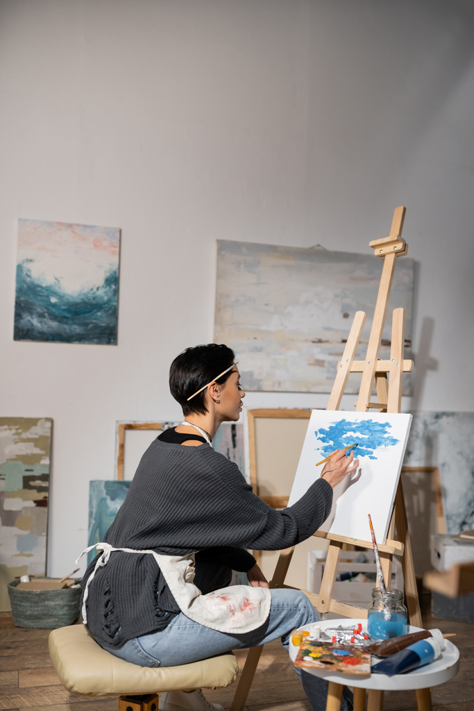Side view of artist in apron painting on canvas in studio  - Photo, Image