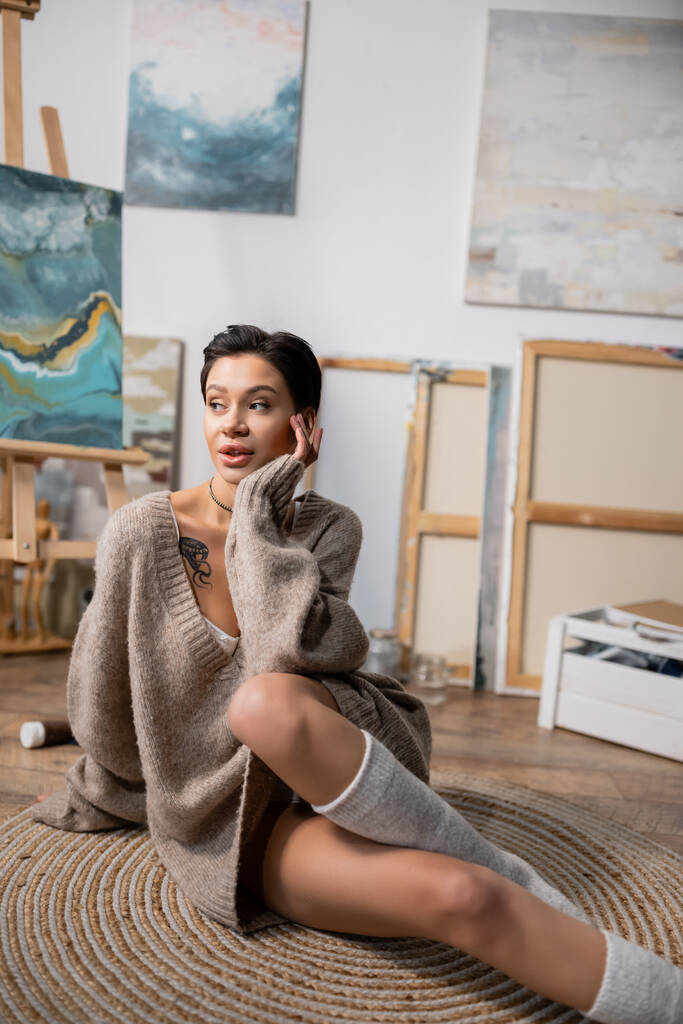 Short haired artist in sweater sitting on floor in studio  - Photo, Image